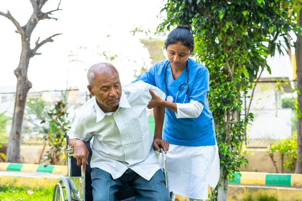 Caregiver or nurse helping senior patient to get up from wheel chair at hospital garden - concept of healthcare assistant, treatment and rehabilitation. — Stock Photo, Image