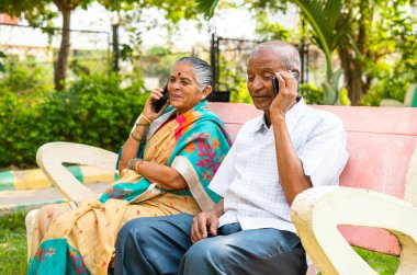 Üst düzey çift parkta otururken cep telefonuyla konuşmakla meşgul - iletişim, tehnoloji, bağlantı ve bağlanma kavramı.