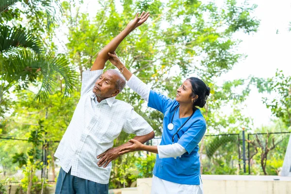 Nurse helping senior old man helping to do exercise at nursing home - concept of caretaker, well-being and rehabilitation — Stock Photo, Image