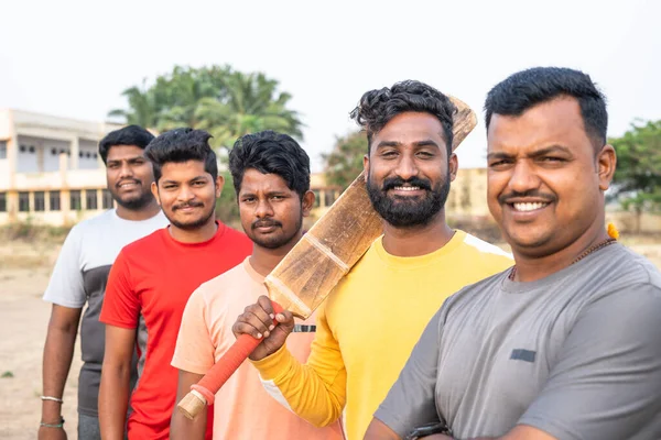 Focus on batsman, Batsman looking camera by holding bat while standing with cricket team - conept of local players, athletics and competition — стоковое фото