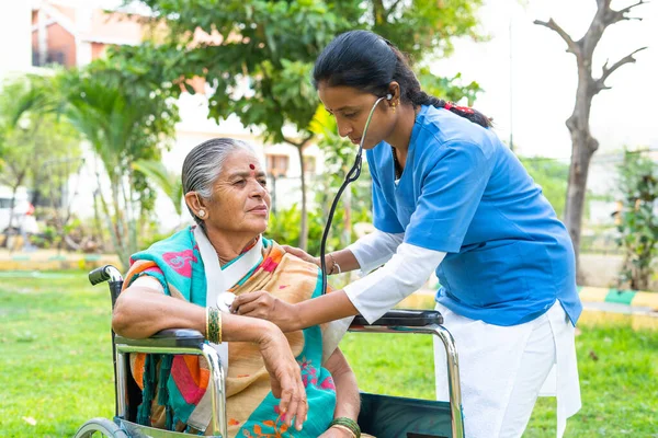 Hemşire, hastane parkında tekerlekli sandalyeli yaşlı bir kadının sağlığını kontrol etmekle ya da izlemekle meşgul. Sağlık, mesleki meslek ve bakıcılık kavramı..