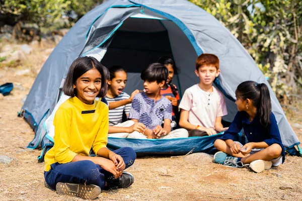 Girl kid looking at camera while talking with friends at camaping tent during summer vacation - concept of happines, outdoor activities, bonding and friendship. — Stock Photo, Image