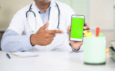 Doktorun yeşil ekran cep telefonunu kamerayı işaret ederek gösteren yakın plan görüntüsü - uygulamanın internet üzerinden tıbbi kontrolünün onaylanması.