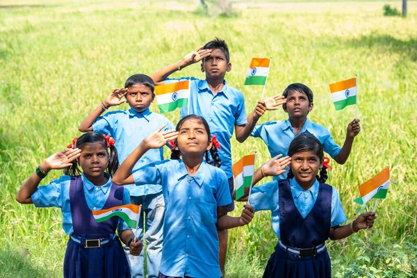 Ομάδα μαθητών του χωριού με ινδική σημαία στο χέρι χαιρετισμό κοιτάζοντας πάνω κατά τη διάρκεια φιλοξενία σημαία - έννοια της ανεξαρτησίας ή ρεπουμπλικανική γιορτή — Φωτογραφία Αρχείου