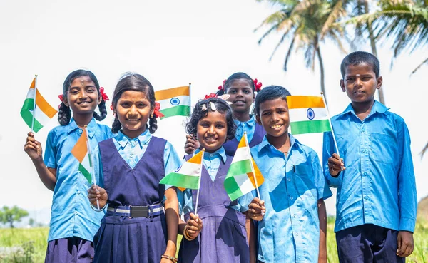 Ομάδα χαρούμενων χαμογελαστών μαθητών του χωριού με στολή που κρατούν τη σημαία των Ινδιάνων κοιτάζοντας την κάμερα κατά τη διάρκεια των εορτασμών της ημέρας ανεξαρτησίας - έννοια του πατριωτισμού, της ποικιλομορφίας και των πραγματικών ανθρώπων. — Φωτογραφία Αρχείου