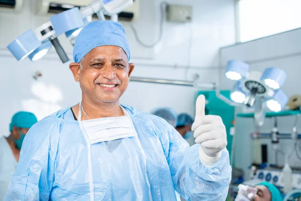 Щасливий усміхнений хірург у формі, що показує великий палець на операційному театрі концепція успішного лікування, затвердження та реклами — стокове фото