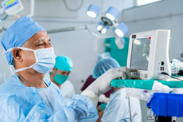 Хирург в форме с помощью монитора для операции пациенту в операционной - концепция технологии, здравоохранения и лечения — стоковое фото
