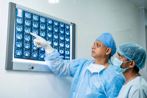 Лікарі у сукнях, що аналізують рентгенівський звіт перед виконанням операції в хірургічному відділенні - зупинилися на медичній експертизі, вивченні та медикаментозному — стокове фото
