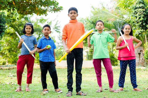 Grupo de niños adolescentes con bate, pelota y muñones listos para jugar cricket mirando la cámara en el parque - concepto de confianza, estilo de vida infantil y actividades de ocio —  Fotos de Stock
