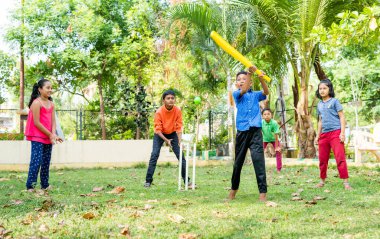 Parkta skor yapmak için kriket oynarken topa vurarak koşan genç bir çocuk - çocukluk fiziksel aktiviteleri, canlılık ve eğlence bağlamında