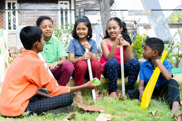 Happy teenager kids having chat with each other after playing cricket while sitting on park - concept of taking break, friendship and socializing. — Stock Photo, Image