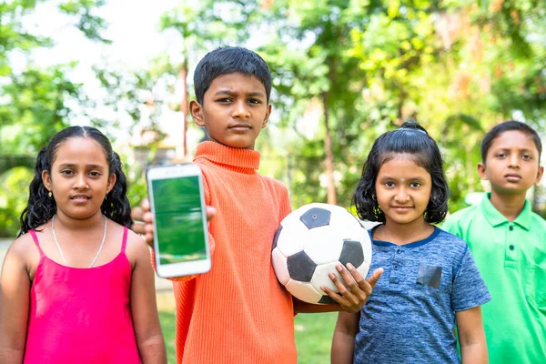 Kid showing green screen mobile phone with football by looking camera with friends - concept of advertisement for training, teamwork and promotion — Stock Photo, Image