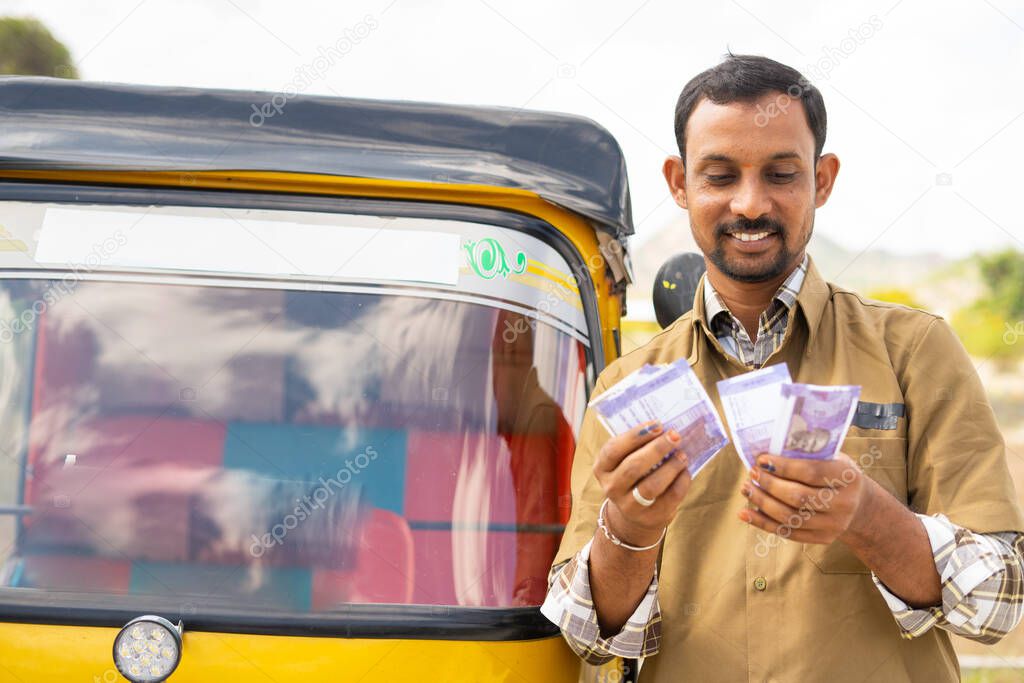 Happy smiling auto Rickshaw driver counting money while standing next to auto - concept of successful business, financial, banking and self employment