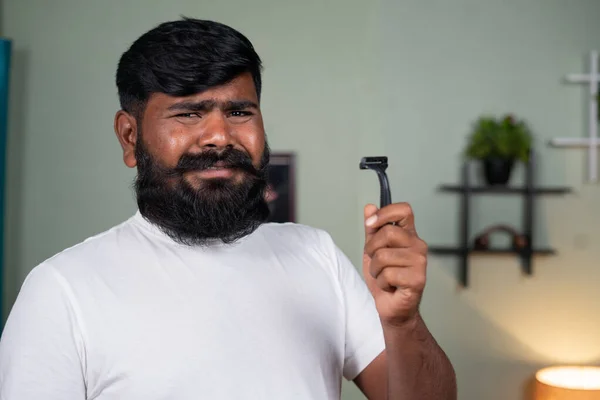 Young man saying no to shave the beard by holding razor and nodding head by looking at camera - concept of grooming and noshavember — Stockfoto