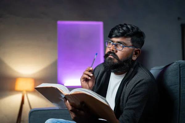 Jeune homme barbe indienne penser tout en lisant le livre la nuit concept de réflexion et d'imagination sur le roman ou la littérature. — Photo