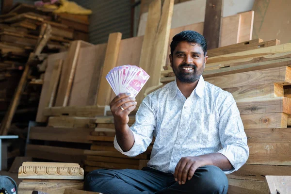 Gelukkige jonge Indiase timmerman met geld of bankbiljetten in Indiase valuta door te kijken naar camera - concept van professionele bezetting, inkomsten, winst in het bedrijfsleven en financiën. — Stockfoto