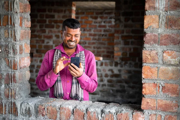 Happy smiling young indian labour busy on mobile phone at workplace - concept of using social media application, technology and leisure activity. — Stockfoto