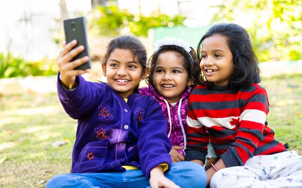 Young girl kids busy making video call on mobile phone at park - concept of social media, technology, internet and childhood friendship — Stock Photo, Image