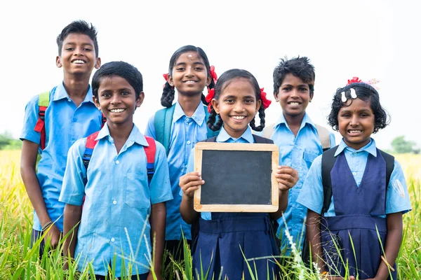 Village teenage kids showing empty slate board by looking at camera at farmland - concept of advertisement, education and friendship — Stock Photo, Image