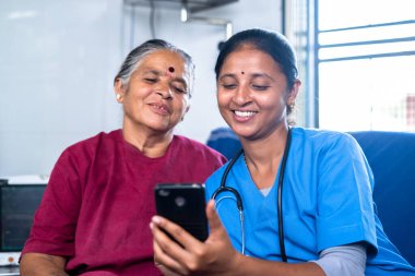 Hastanede cep telefonu izleyerek gülen mutlu, mutlu, hasta, son sınıf öğrencisi bir kadına odaklanmak. Teknoloji, rahatlama ve bakıcı kavramı.