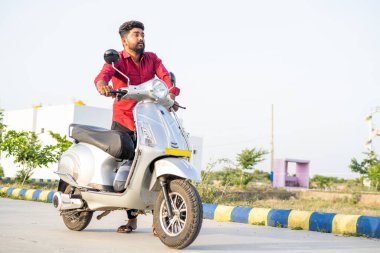 Düşük batarya ve motor arızası konsepti yüzünden Ev 'i iten endişeli genç adamın tam karesi veya elektrikli scooter ile yol kurutma seyahati