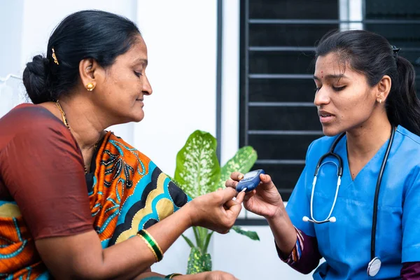 Nurse at home checking diabetes of sick middled aged woman at home using glucometer - concept of home health checkup, caretaker and occupation