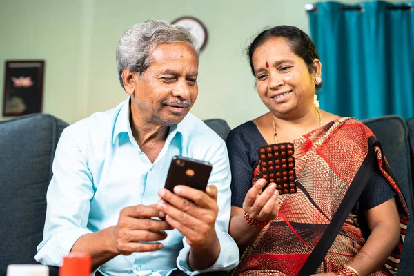 senior old couple ordering medicines on mobile phone application while sitting on sofa at home - concept of Healthcare, online technology and e-commerce.