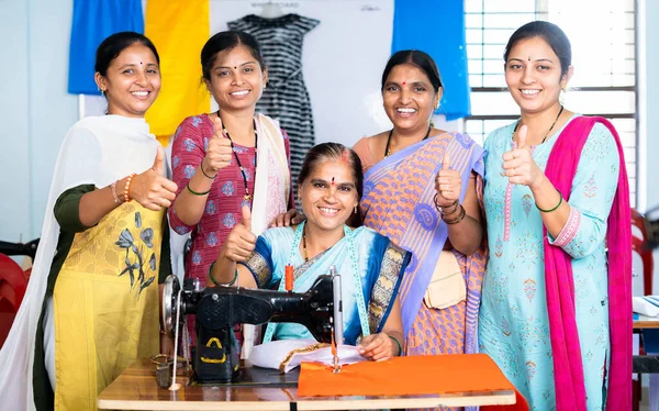 Woman with trainers around showing thumbs up by looking at camera while learning tailoring at class - concept of woman empowerment, growth and development
