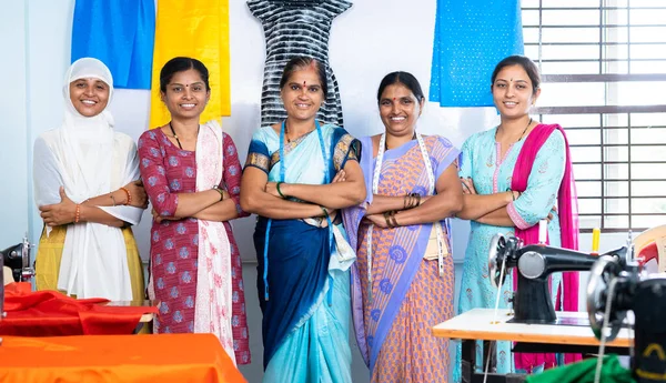 Team of confident woman woman workers at garment standing by arms crossed behind the sewing maching - concept of small business, community growth and development.