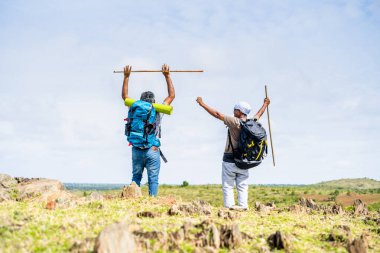 Yürüyüşçülerin kutlama görüntüsü, hedefe ulaştıktan sonra tepenin üstünde sopayla el kaldırarak - başarılı yolculuk, hedef ve mutluluk kavramı.
