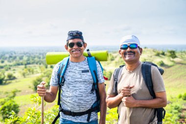Sırt çantalı mutlu yürüyüşçüler ya da dağda yürürken kameraya bakan gezginler - arkadaşlık, rahatlama ve boş zaman aktiviteleri kavramı.