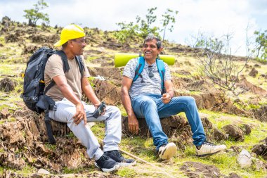 Mutluluk, dostluk ve seyahat konsepti, tepenin üstünde otururken mola için yürüyüş yaparken birbirleriyle konuşan mutlu yürüyüşçüler.