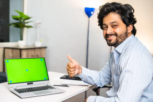 Happy young man with green screen laptop showing thumbs up by looking camera at office - concept of career promotion, advertisement and employment.