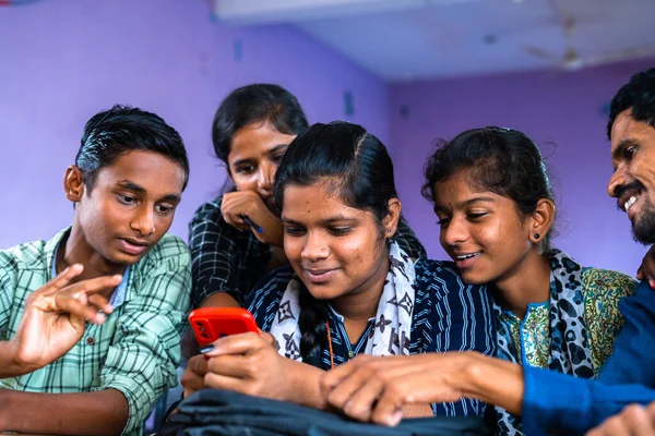 Group of excited college students checking exam results on mobile phone at classroom - concept of education, friendship and happiness.