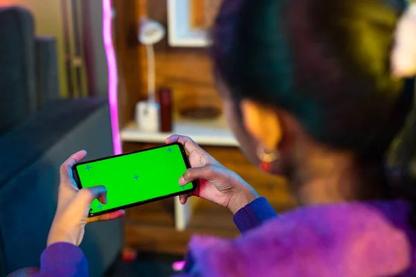Shoulder shot of teenager girl playing video game on green screen mobile phone at home - concept of enteraiment, gaming addiction and technology.