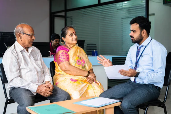 Focus on banker, Bank employee explaining about insurance or loan policy to senior couple at office - concept of financial support, banking consultant and assistance.