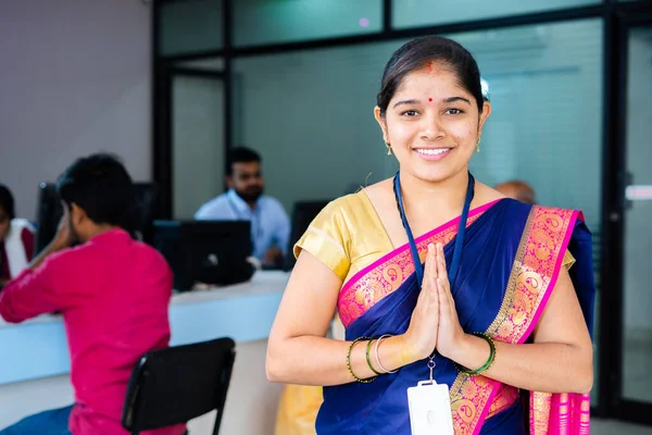 Portrait shot of Happy smiling bank employee greeting by doing namaste while looking camera in front of customers - concept of gratitude, welcome gesture and custimer service