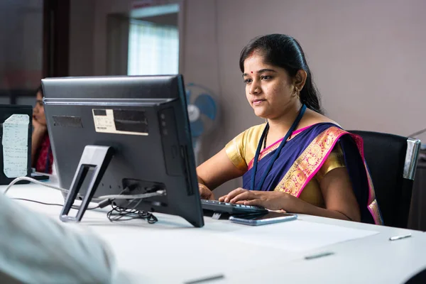 Serious bank employee busy working on computer in front of customer - concept of woman empowerment, job or career and banking service