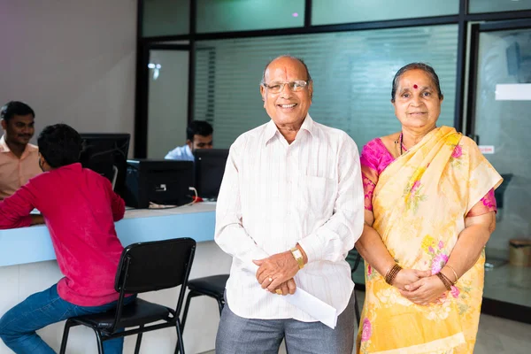 Portrait of Happy smiling senior couple standing by looking camera at bank - concept of customer service, elderly investment and financial support
