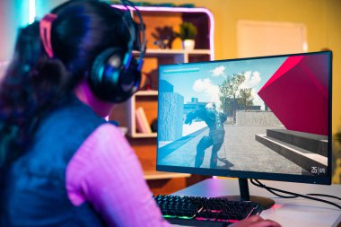 shoulder shot of gamer playing online video game on computer by talking on headphones at home - concept of competition, entertainment and professional.