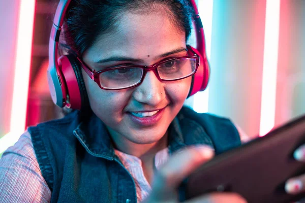 Close up shot of girl with headphones and eyeglass playing online video game on mobile phone at home - concept of live streamer, holydays and cyberspace.