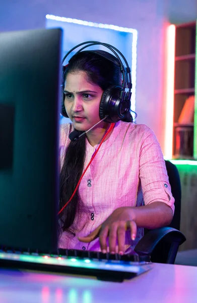Woman playing live video game on computer by talking to players on headphones at home - concept of live streamer, vlogger and tournament