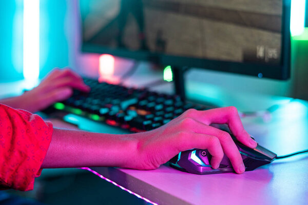 Close up shot of teenager kid hands using mouse while playing video game at neon light background - concept of entertainment, hobbies and technology