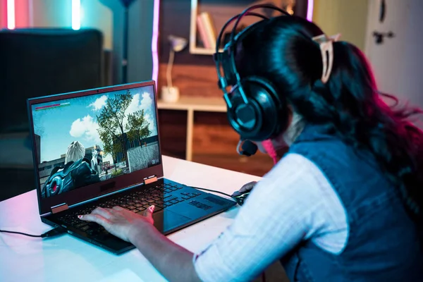 Shoulder shot of woman with headphones playing online video game on laptop at home - concept of live streaming, competitive and technology