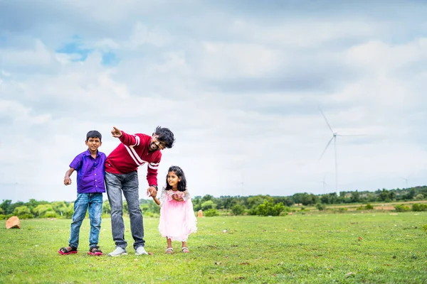 Happy indian father enjoying weekend with kid and showing wind fan at power station - concept of weekend, bonding and renewable energy