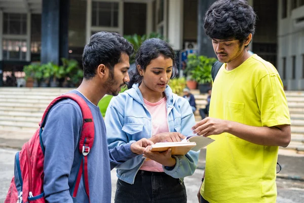 group of young indian Students busy on by discussing of syllabus during examination at college campus - concept of learning discussion and friendship.