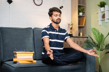 Genç Hintli öğrenci evde çalışmaya hazırlanmadan önce meditasyon yapıyor - meditasyon konsepti, sağlıklı yaşam tarzı ve stres atağı.