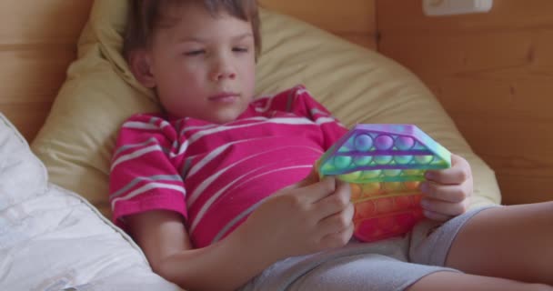 Малюк лежить на ліжку і грає з Поп-Він — стокове відео