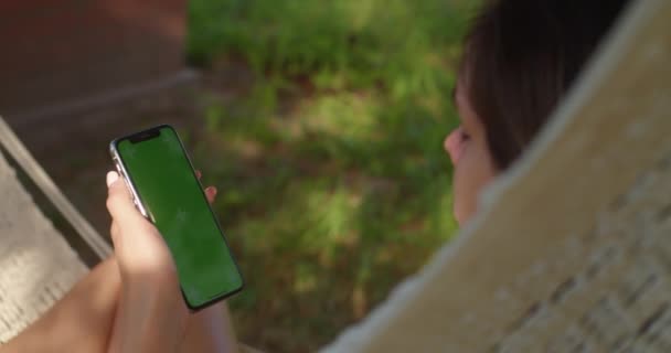 Młode kobiety odpoczywają w hamaku patrząc na telefon z zielonym ekranem — Wideo stockowe