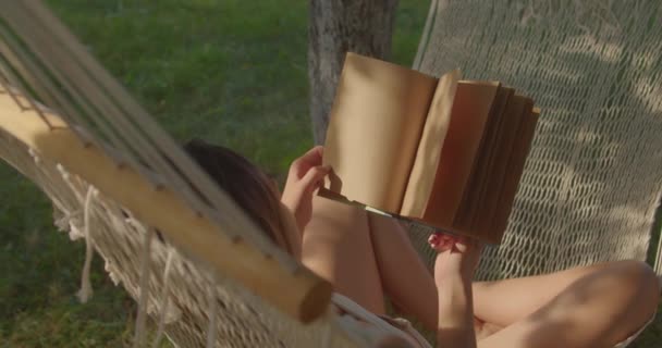 Tiener meisje heeft rust in geweven hangmat lezen boek — Stockvideo